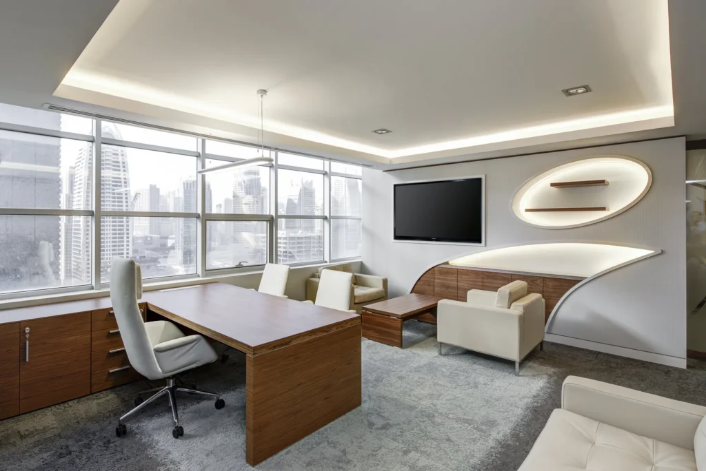 Escritório sofisticado com mesas planejadas para escritório, cadeiras elegantes, estante embutida e vista urbana através de janelas amplas.